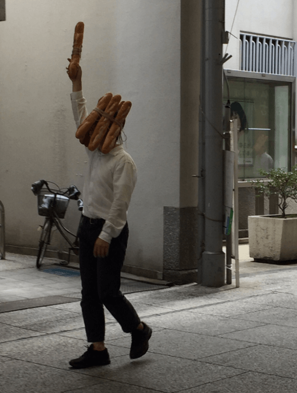 フランスパンを頭にくくり付け歩く男性の画像